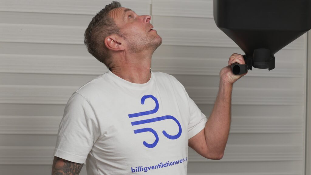 Mand i T-shirt inspicerer ventilationsanlæg, klar til rens